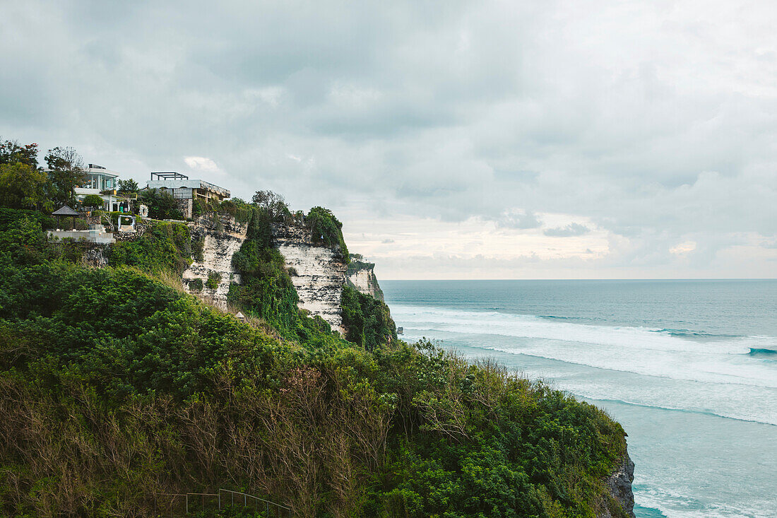 Oceanfront beach houses on the cliffs of the Bukit Peninsula at Uluwatu Beach, looking out to the Indian Ocean in South Bali on a cloudy day; Uluwatu, Badung, Bali, Indonesia