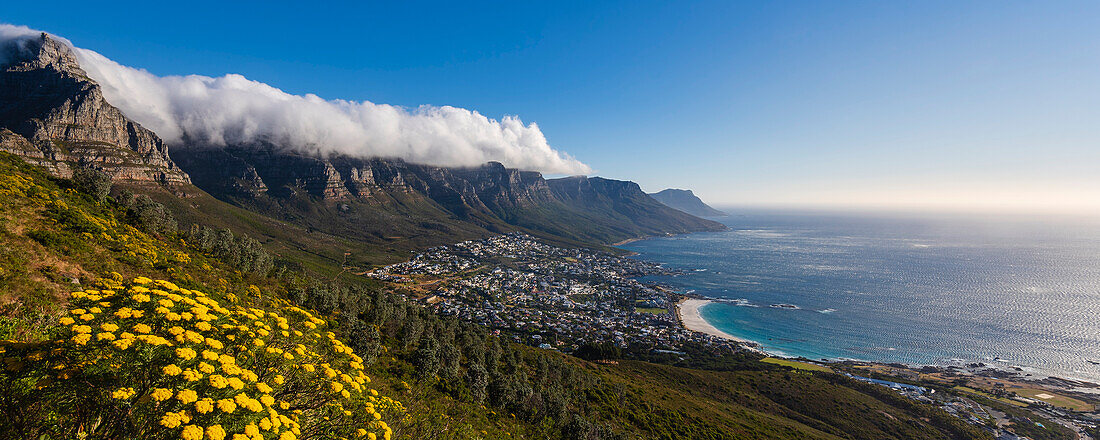 Wolkenformation, die den Tischtuch-Effekt über der Bergkette der Zwölf Apostel erzeugt, mit Blick auf die Skyline von Kapstadt und die Camps Bay entlang der Atlantikküste; Kapstadt, Provinz Westkap, Südafrika