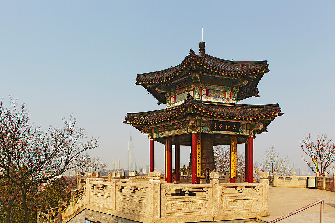 A traditional bell tower pavilion at Jiuhuashan Temple with the modern city in the background, near Xuanwu Lake, Nanjing, Jiangsu province, China.; Jiuhuashan Temple, Nanjing, Jiangsu province, China.