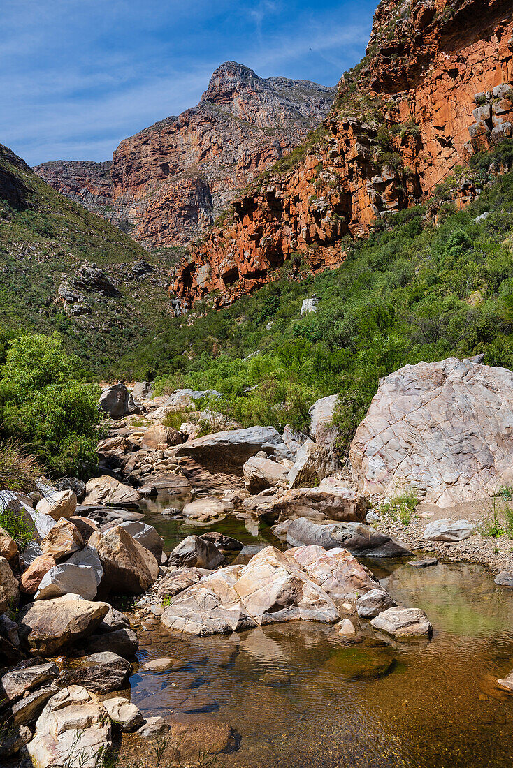 View of a mountain peak through rocky cliffs with a stream surrounded by boulders in the foreground; Western Cape, South Africa