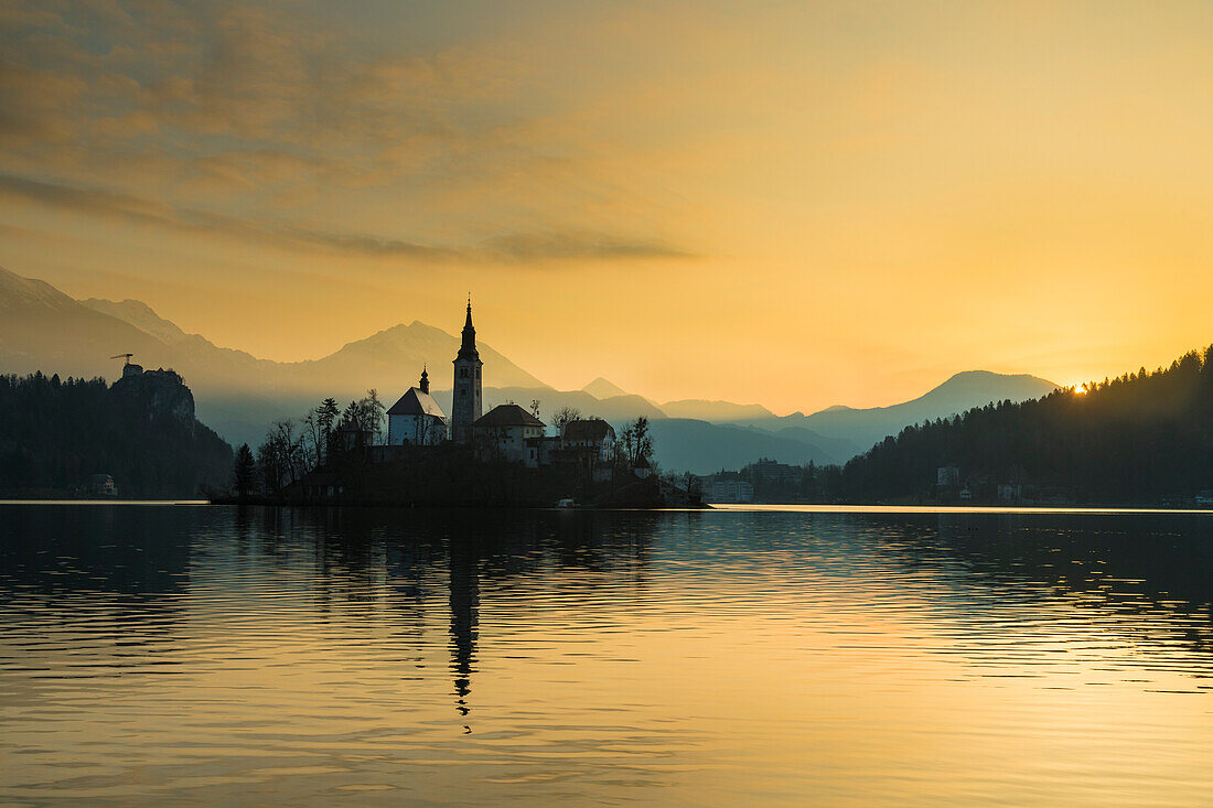 Silhouette der Kirche und anderer Gebäude am Bleder See in der Morgendämmerung; Bled, Slowenien