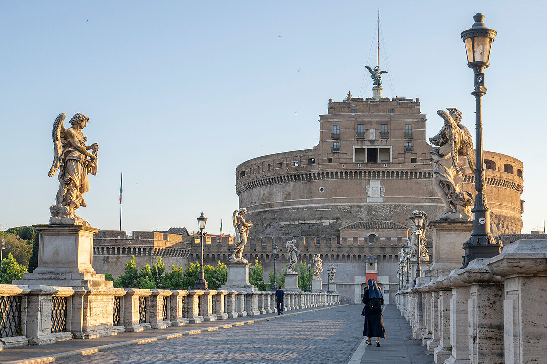 View of the Castel Sant'Angelo (Mausoleum of Hadrian) with a pedestrian and a Nun crossing the Ponte Sant'Angelo; Rome, Lazio, Italy