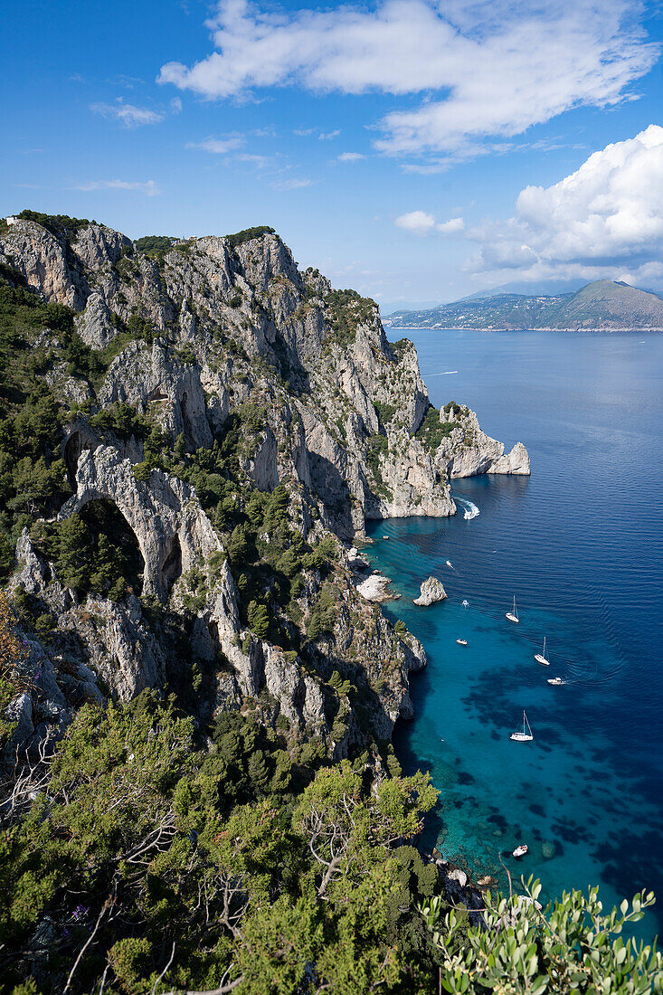 View from the rocky cliffs on the Island of Capri over the Amalfi Coast and the Bay of Naples with boats moored off the shoreline; Naples, Capri, Italy