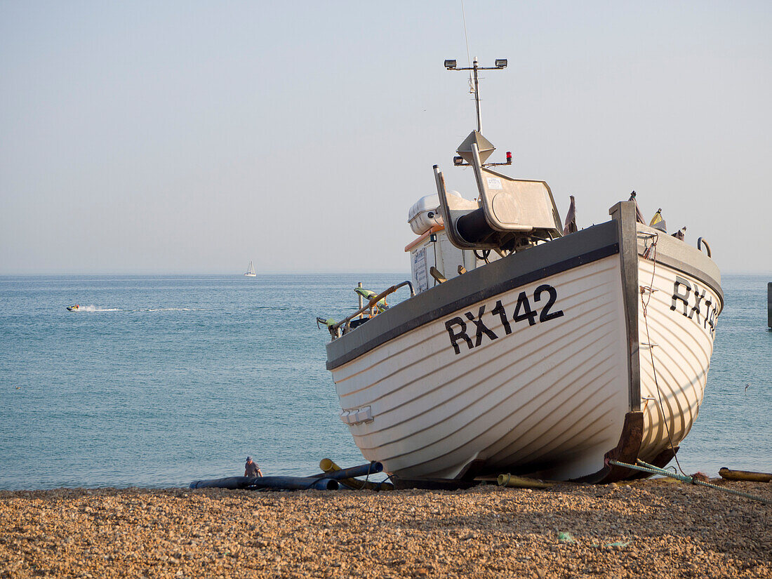 Hölzernes Fischerboot am Ufer des Kieselstrandes mit Meer im Hintergrund; Hastings, East Sussex, England, Vereinigtes Königreich