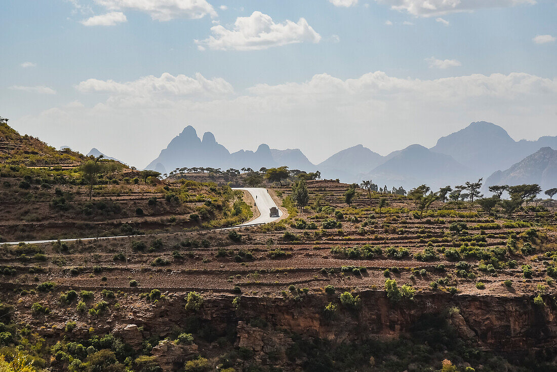Ländliche Szene mit terrassiertem Ackerland und einem Lastwagen, der eine Bergstraße im äthiopischen Hochland entlangfährt; Äthiopien