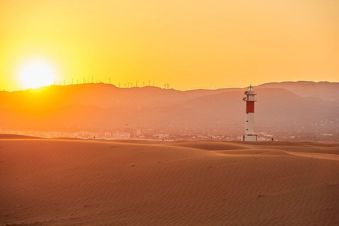 Lighthouse with red stripe on the rippled sand dunes in the evening light at sunset, Ebro River Delta; Catalonia, Spain