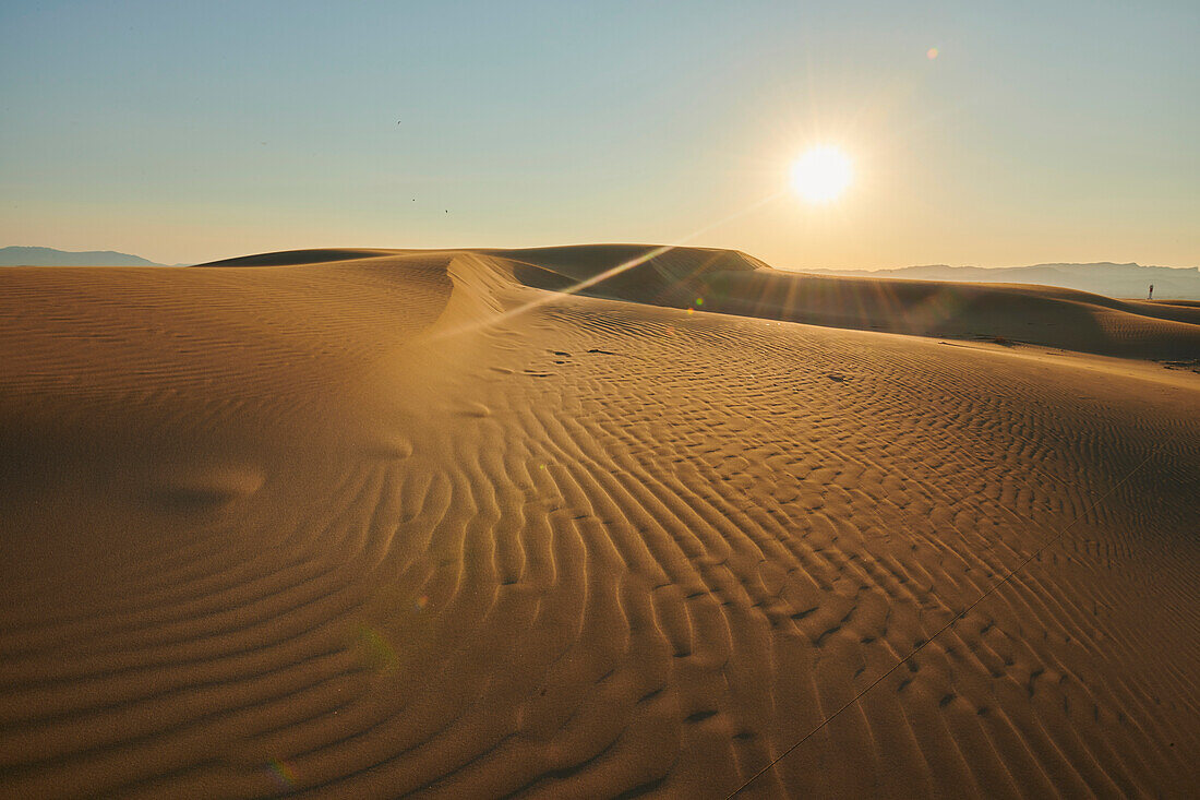 Rippled sand dunes in the evening light at sunset, with a lighthouse in the distance, Ebro River Delta; Catalonia, Spain