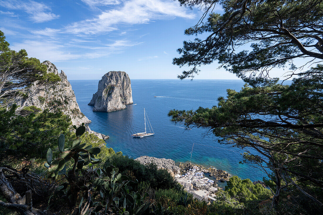 View of Faraglioni Bay and Rock formation with sailboat moored along the shore in the Bay of Naples off the Island of Capri; Naples, Capri, Italy
