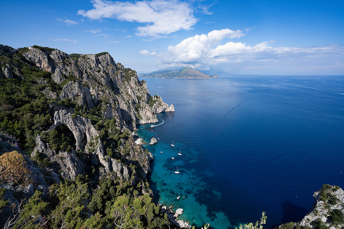 View from the rocky cliffs on the Island of Capri over the Amalfi Coast and the Bay of Naples with boats moored off the shoreline; Naples, Capri, Italy