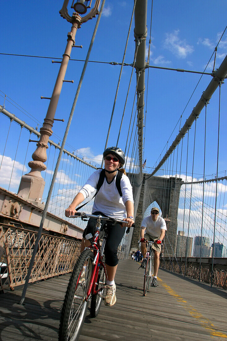 Couple biking across the Brooklyn Bridge in New York City.; Brooklyn Bridge, New York.