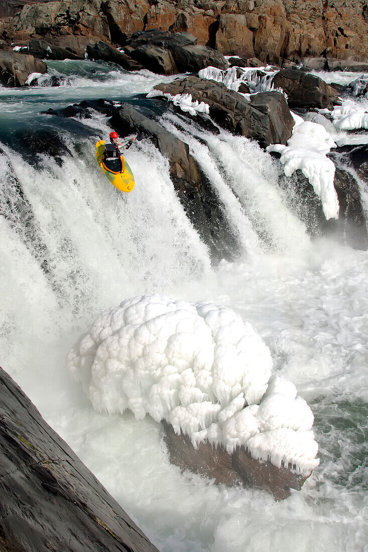 Winter whitewater kayaker on the verge of a big waterfall with ice.; Great Falls, Potomac River, Maryland.