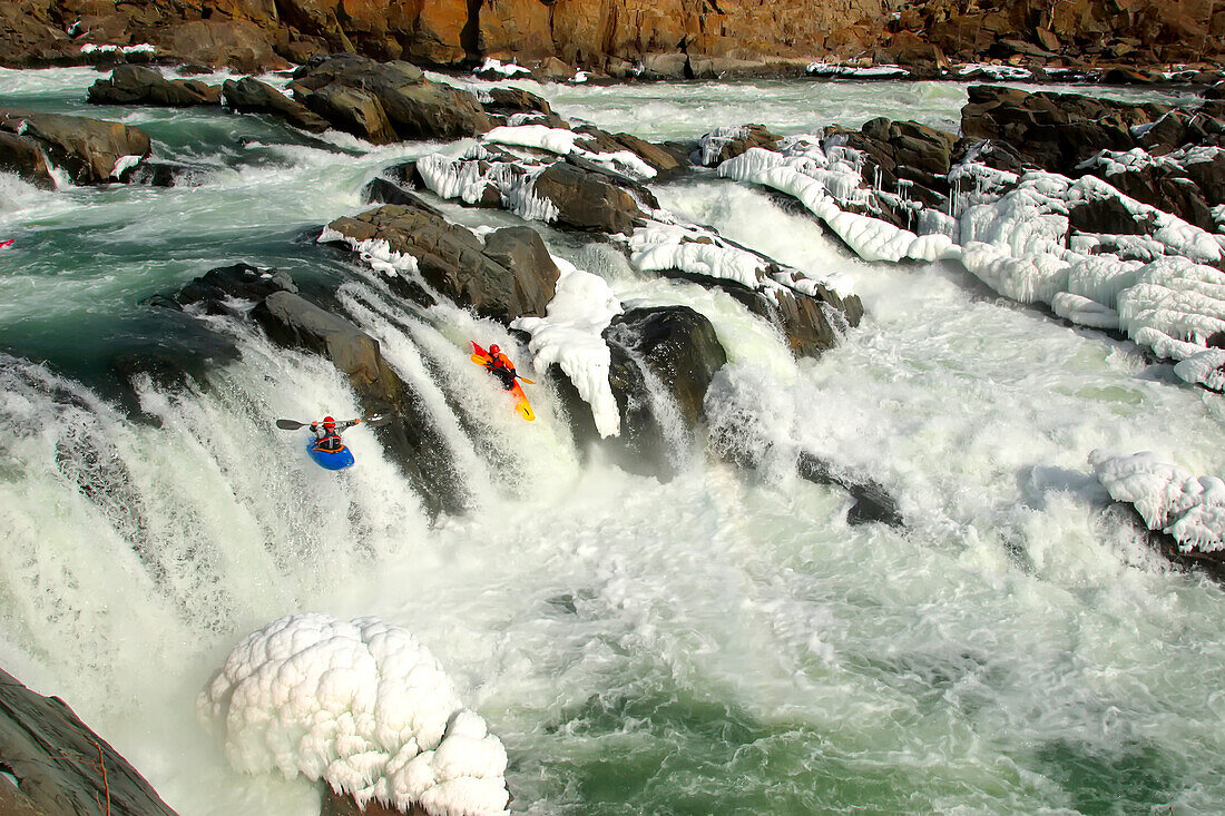 Two whitewater kayakers paddle together off nearly frozen waterfalls.; Great Falls, Potomac River, Maryland.