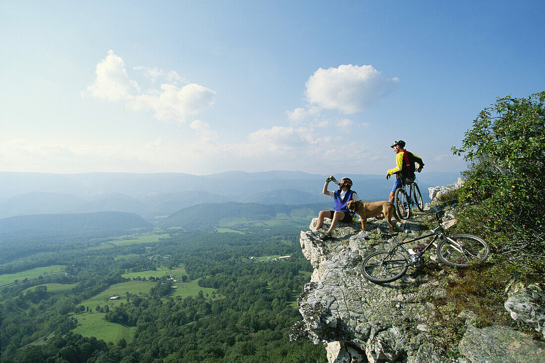 Mountains bikers and their dog rest on the edge of a cliff.; Germany Valley, West Virginia.