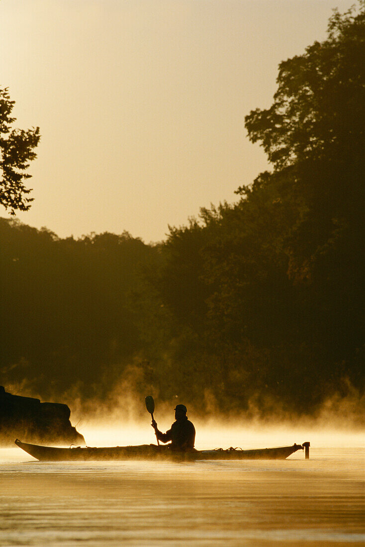 A kayaker paddles through mist rising from the Potomac River at dawn.; Potomac River, Maryland.