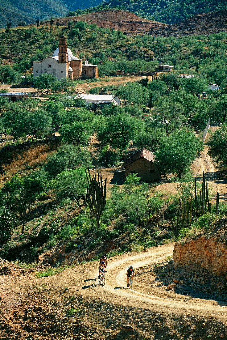 Mountainbiker fahren von Batopillas los, dahinter die Satevo Mission; Copper Canyon, Mexiko.