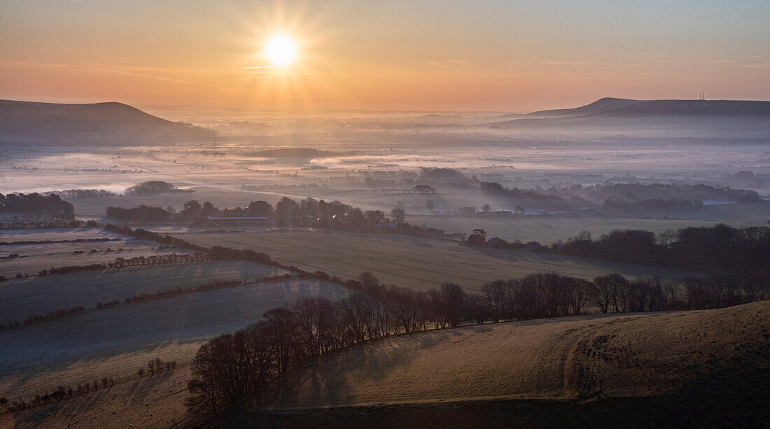 The sunrise casts long shadows over a morning mist inversion lying over the English countryside in South Downs National Park; Lewes, East Sussex, England
