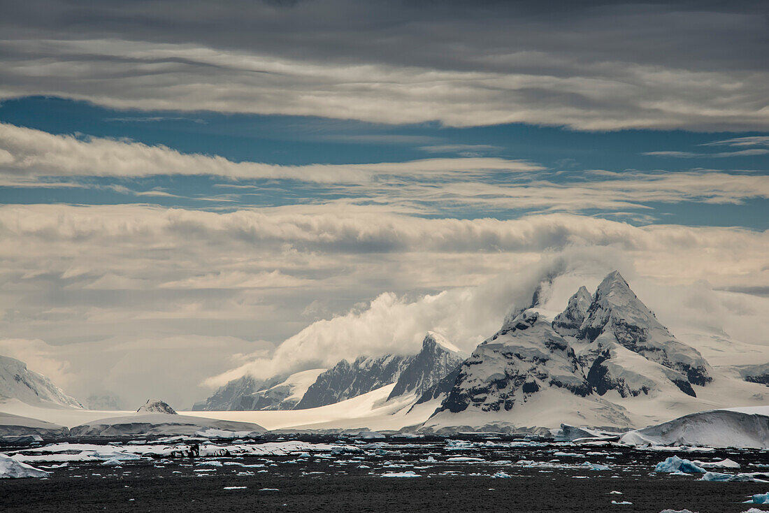 Mountainous, snow covered landscape on Booth Island along the icy ocean coastline, home to colonies of Gentoo, Adelie and Chinstrap Penguins; Antarctica