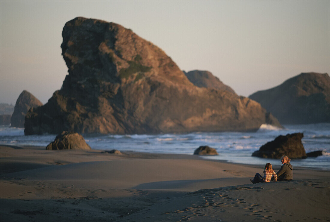 Zwei Menschen unterhalten sich in der Dämmerung am felsigen Strand; Pistol River, Oregon.