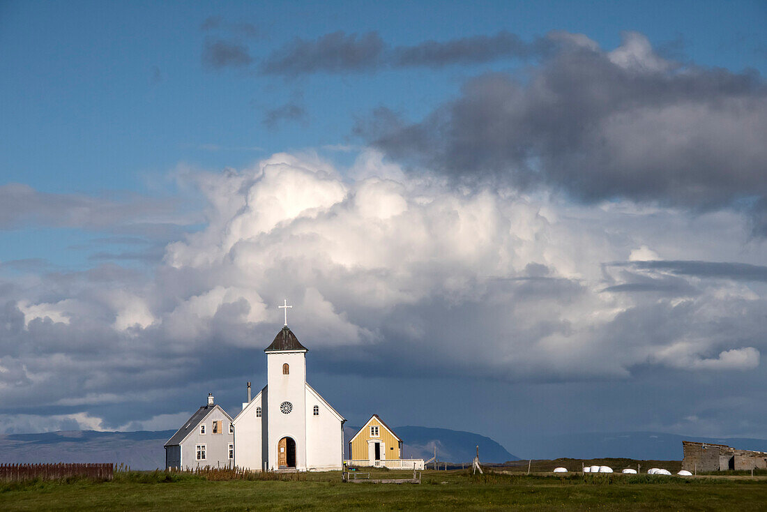 Community church illuminated by the sun with a cloudy sky over Flatey Island, part of a cluster of about forty large and small islands and islets located in Breiðafjörður on the northwestern part of Iceland; Western Islands, Iceland