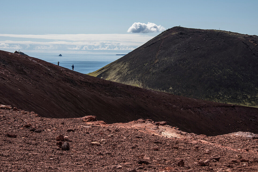 People walking on the volcanic slopes exploring the volcano, Eldfell, on the island of Heimaey, part of the Westman Islands, an archipelago of some 15 islands on the South Coast of Iceland, formed some 11,000 years ago. The volcano exploded on January 23, 1973, when the entire island was evacuated, except for 300 people who stayed behind to fight the lava flow with water hoses; Heimaey Island, Iceland