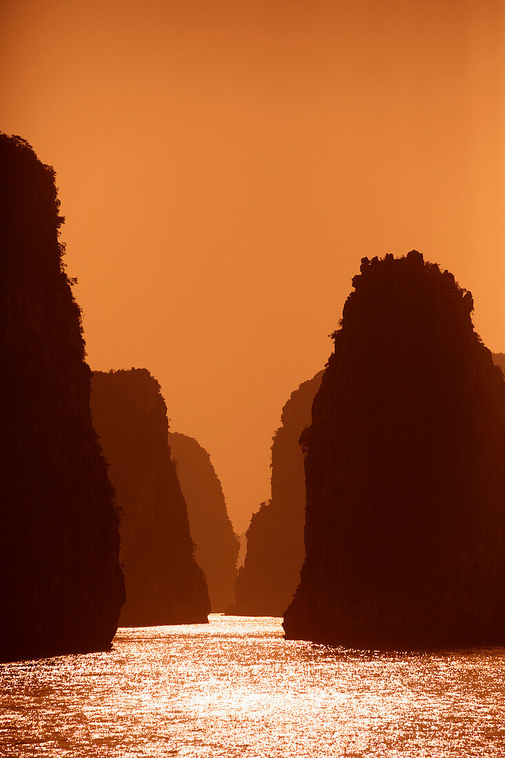 Karstformationen und glitzernder, sonnenbeschienener Ozean bei Sonnenuntergang in der Bai Tu Long Bucht in der Halong Bucht, die zum UNESCO Weltkulturerbe gehört; Halong Bucht, Quang Ninh, Vietnam