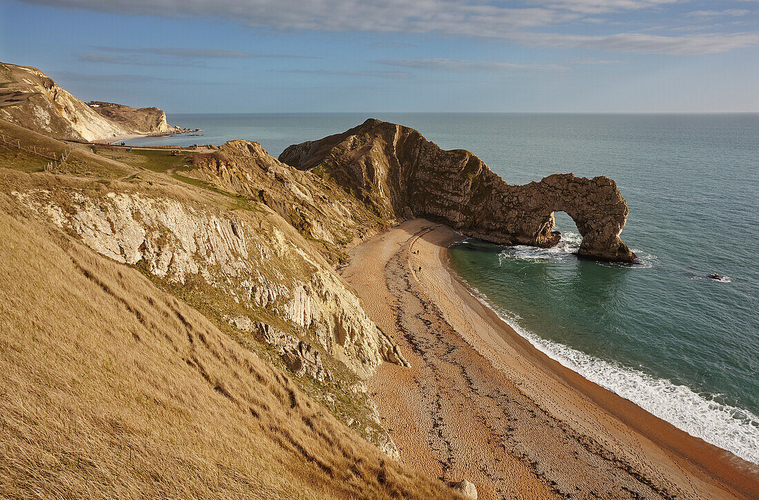 Spaziergänger am Strand mit Blick auf den Atlantischen Ozean und die Durdle Door Felsformation an der Jurassic Coast bei Lulworth; Dorset, England, Großbritannien