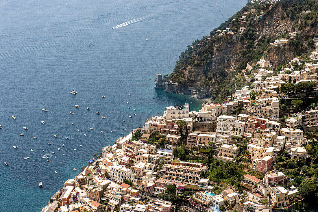 Aerial view of the stone buildings and terraces on the cliffside in the town of Positano with boats moored along the Amalfi Coast; Positano, Salerno, Italy