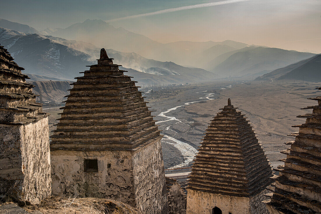 Verlassenes Dorf mit traditionellen kegelgedeckten Hütten am Berghang in Inguschetien, Blick auf die dunstige Berglandschaft darunter; Republik Inguschetien, Russland