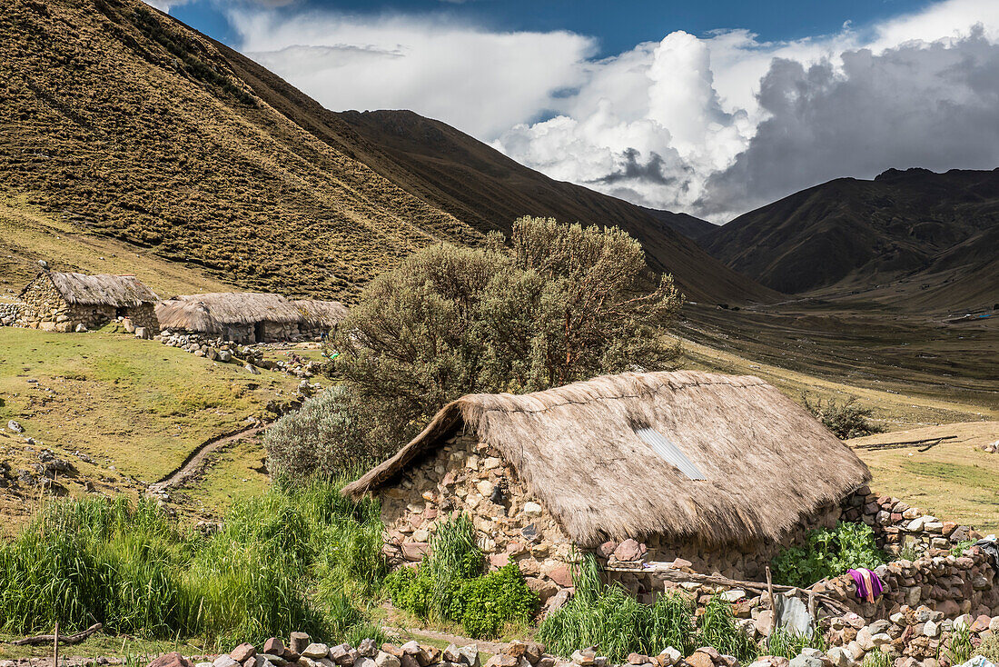 Bauerngemeinschaft im Lares-Tal mit den Anden, die sich über den Steinhäusern mit Strohdächern abzeichnen; Lares-Tal, Cusco, Peru