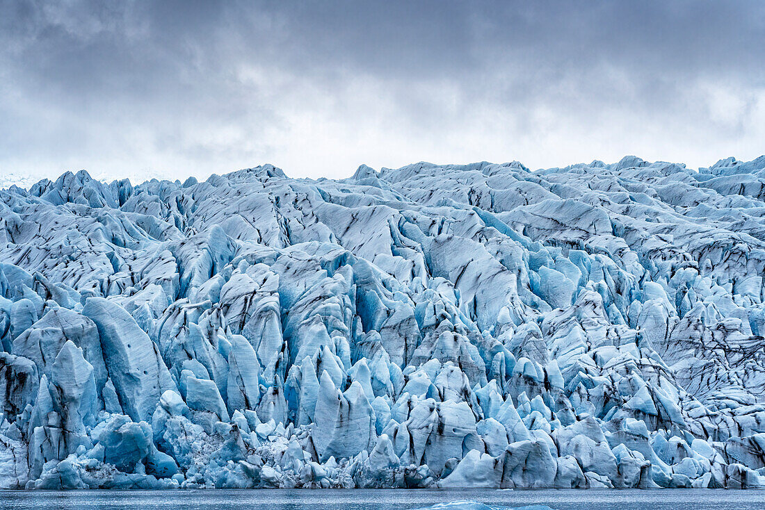 Nahaufnahme aus der Fjallsarlon Gletscherlagune von den zerklüfteten blauen Eisformen des Fjallsjokull Gletschers, der sich von den grauen, nebligen Wolken abhebt, am Südende des berühmten isländischen Gletschers Vatnaj?l in Südisland; Südisland, Island