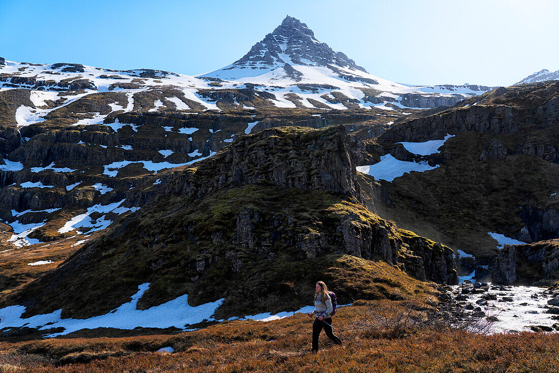 Woman walking alone along a trail beside a river; East Iceland, Iceland