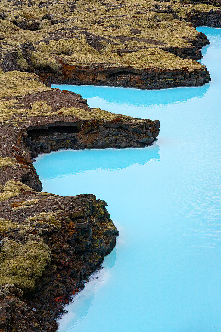 Atemberaubende Luftaufnahme des türkisblauen Wassers, das einen dynamischen Kontrast zu den moosbewachsenen Lavafeldern entlang der Küste von Südisland bildet; Blaue Lagune, Südisland, Island