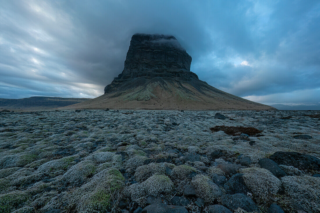 Riesige Steilwand entlang der Südküste Islands bei Sonnenuntergang. Moosbewachsene Felsen im Vordergrund weisen den Weg ins Bild; Südküste, Island