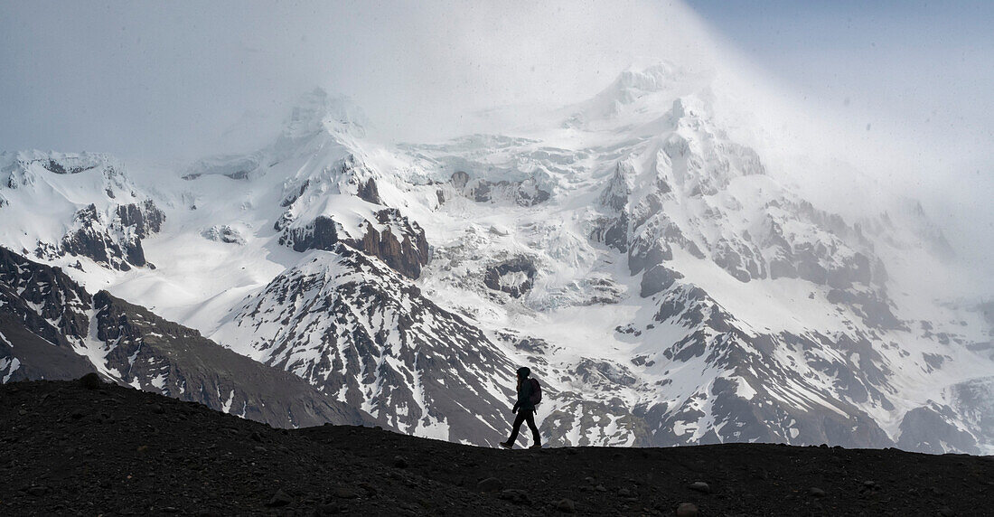 Silhouette einer Person, die entlang einer Gletschermoräne vor einem großen schneebedeckten Berg an der Südküste Islands geht; Südisland, Island