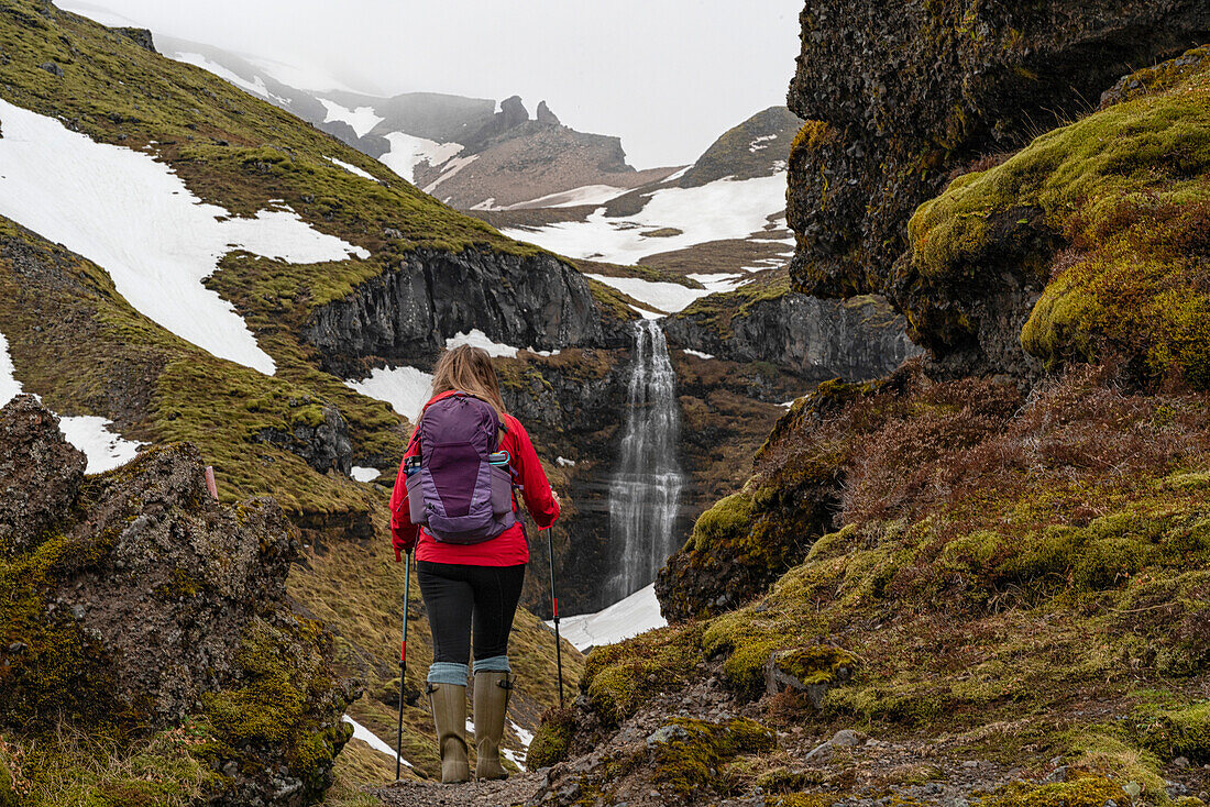 Nahaufnahme, von hinten aufgenommen, einer Frau mit Blick auf den Mulagljufur Canyon, ein Wanderparadies, mit einem erstaunlichen Blick auf einen Wasserfall durch die moosbewachsenen Klippen; Vik, Südisland, Island
