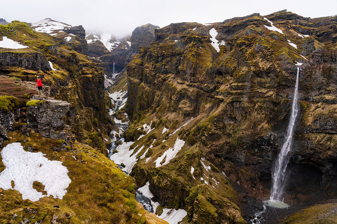 Fernblick einer Frau auf den Mulagljufur Canyon, ein Wanderparadies, mit erstaunlichem Blick auf die Wasserfälle, den Fluss und die moosbewachsenen Klippen; Vik, Südisland, Island