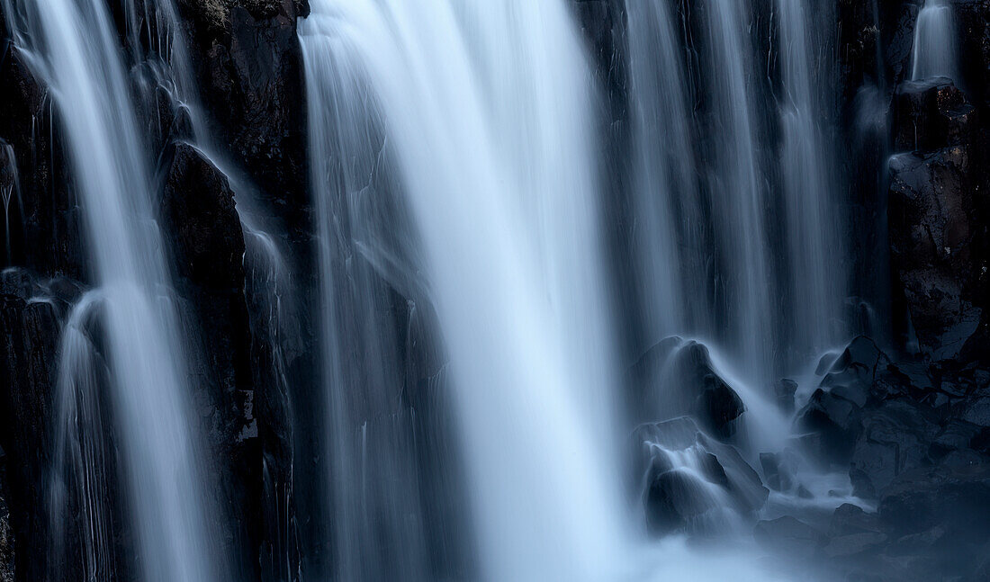 Nahaufnahme einer Reihe von Wasserfällen, das weiche Verschwimmen von fließendem Wasser über schwarzem Fels; Island