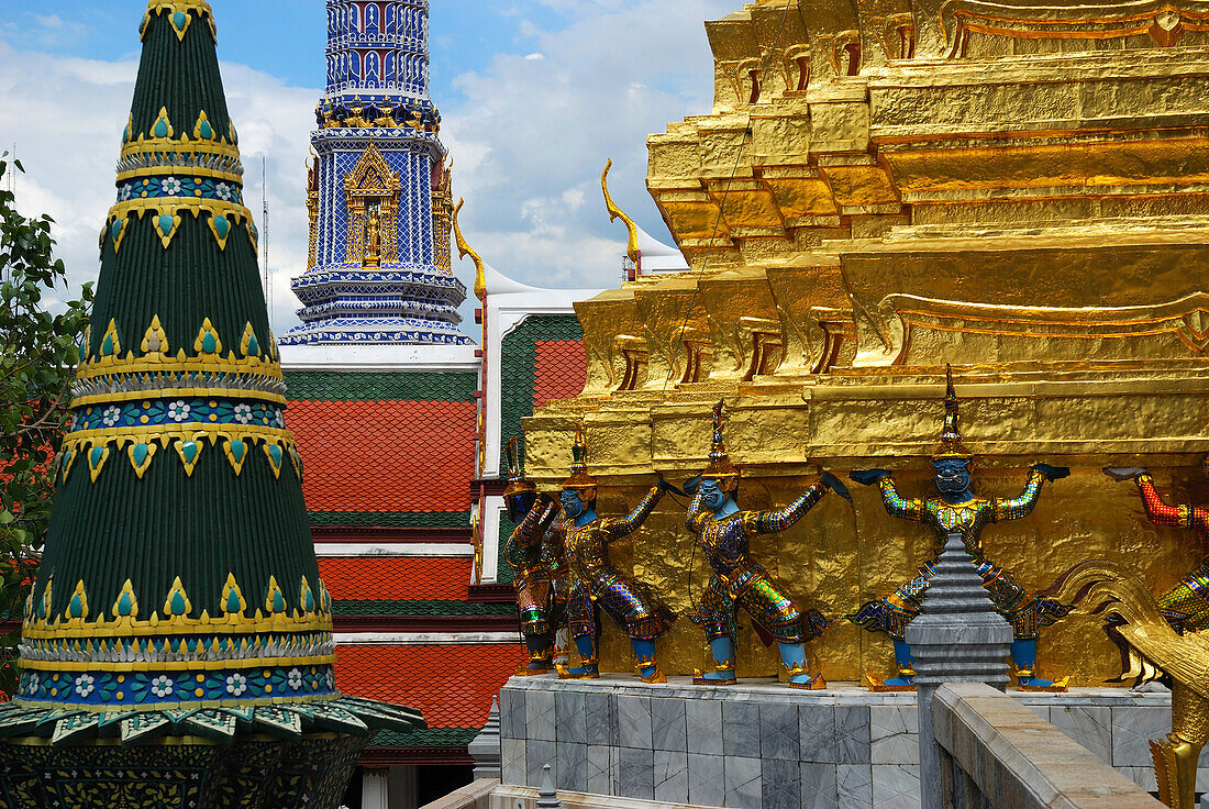 Mosaic-covered spires and a gilded one held up by mythological beings.; Temple of the Emerald Buddha, The Grand Palace, Bangkok, Thailand.
