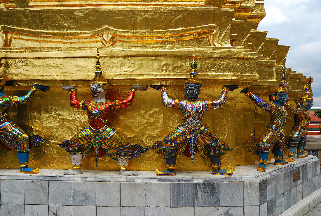 Statues of mythological gods and goddesses circling a gilt temple.; Temple of the Emerald Buddha, The Grand Palace, Bangkok, Thailand.