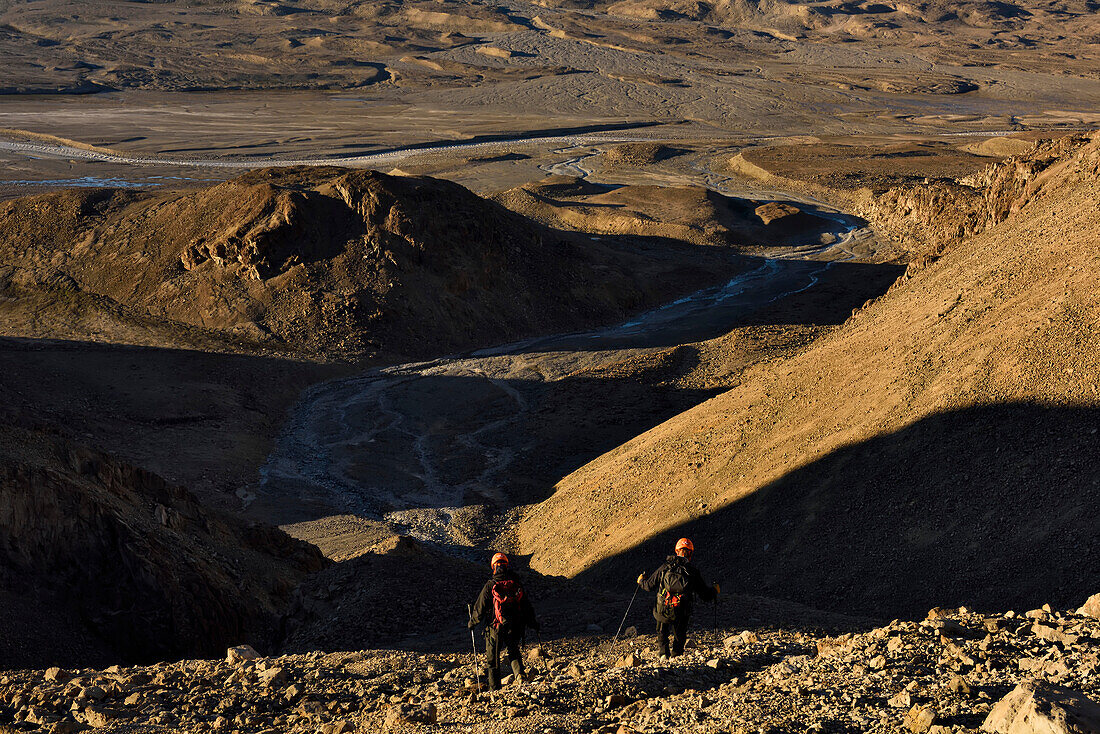 Expedition team members skip down one of the scree slopes of rocks towards the bottom of the valley of the caves and then onto camp to put a pan of water on the stove for tea. Grottedalen looms large in the background