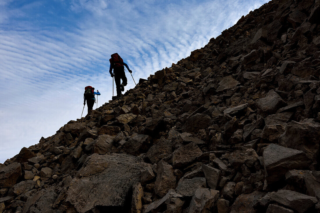 Expedition members climb a scree slope of rocks to explore, survey, photograph, and sample caves of Northeast Greenland for the purpose of climate-change research.