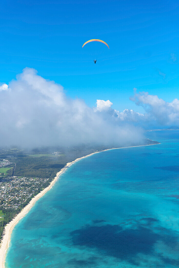 Paraglider flying high over Honolulu coastline with turquoise waters of the Pacific Ocean and a blue sky; Oahu, Hawaii, United States of America