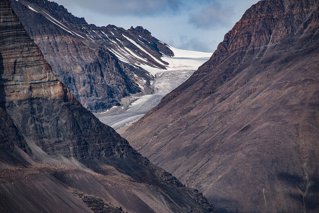 View through the mountainous landscape to an icy glacier mass in the Kong Oscar Fjord of Greenland; East Greenland, Greenland