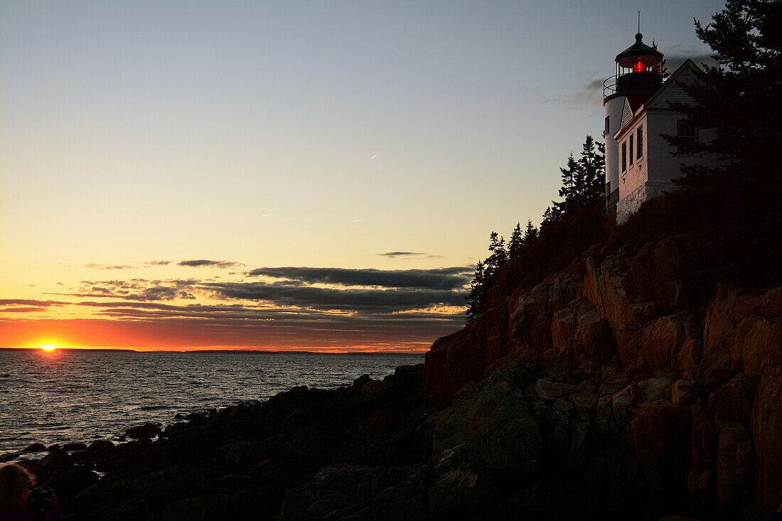 Sunset view of the Bass Harbor Lighthouse and the rocky shoreline in Acadia National Park.; Bass Harbor Head Lighthouse, Acadia National Park, Mount Desert Island, Maine.