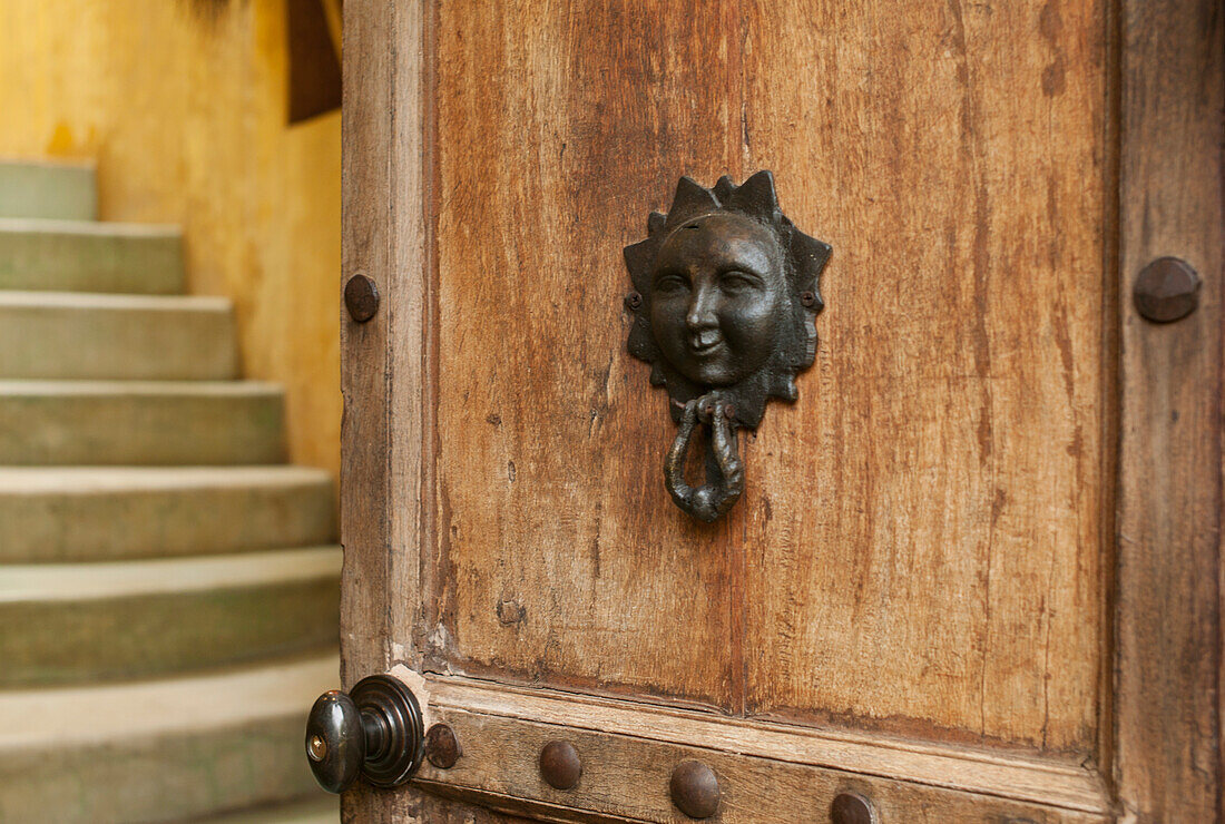 A Door Knocker With The Image Of A Human Face On A Wooden Door; Sayulita Mexico