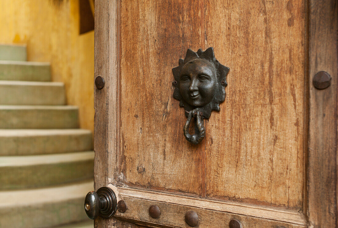 Ein Türklopfer mit dem Bild eines menschlichen Gesichts auf einer Holztür; Sayulita Mexico