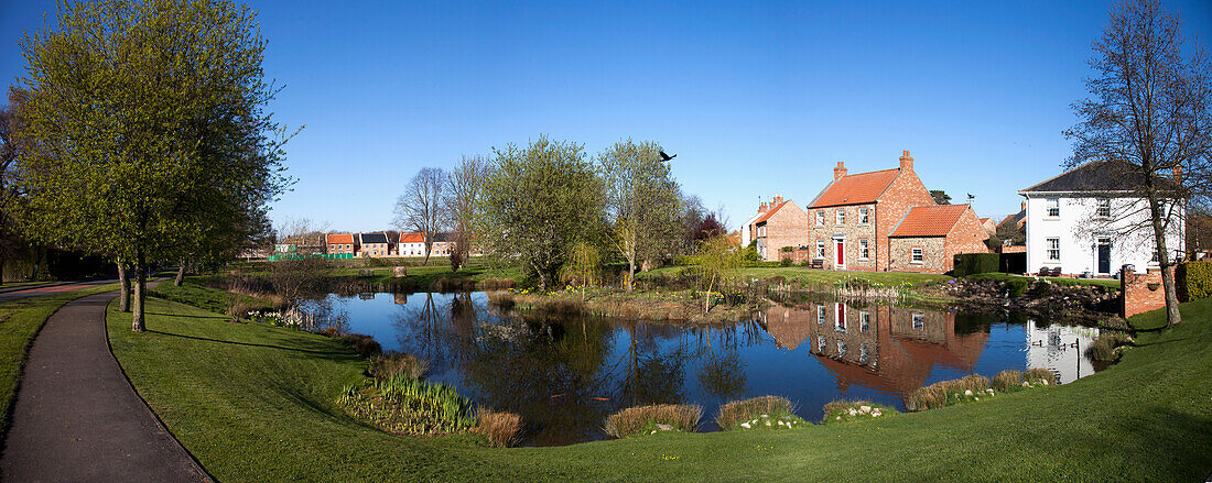 Häuser spiegeln sich in einem ruhigen Teich; East Witton Yorkshire England