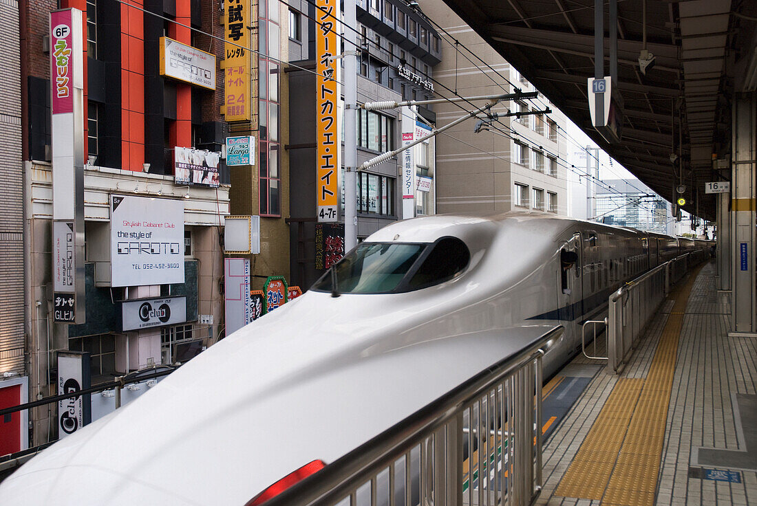 Japanischer Hochgeschwindigkeitszug wartet am Bahnhof mit Gebäuden dicht dahinter; Tokio, Japan