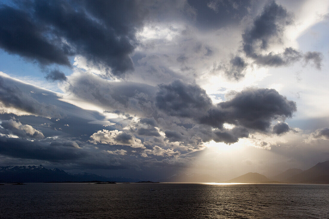 Sonnenlicht, das durch dunkle Wolken auf das Wasser und die Berge an der Küste scheint; Argentinien