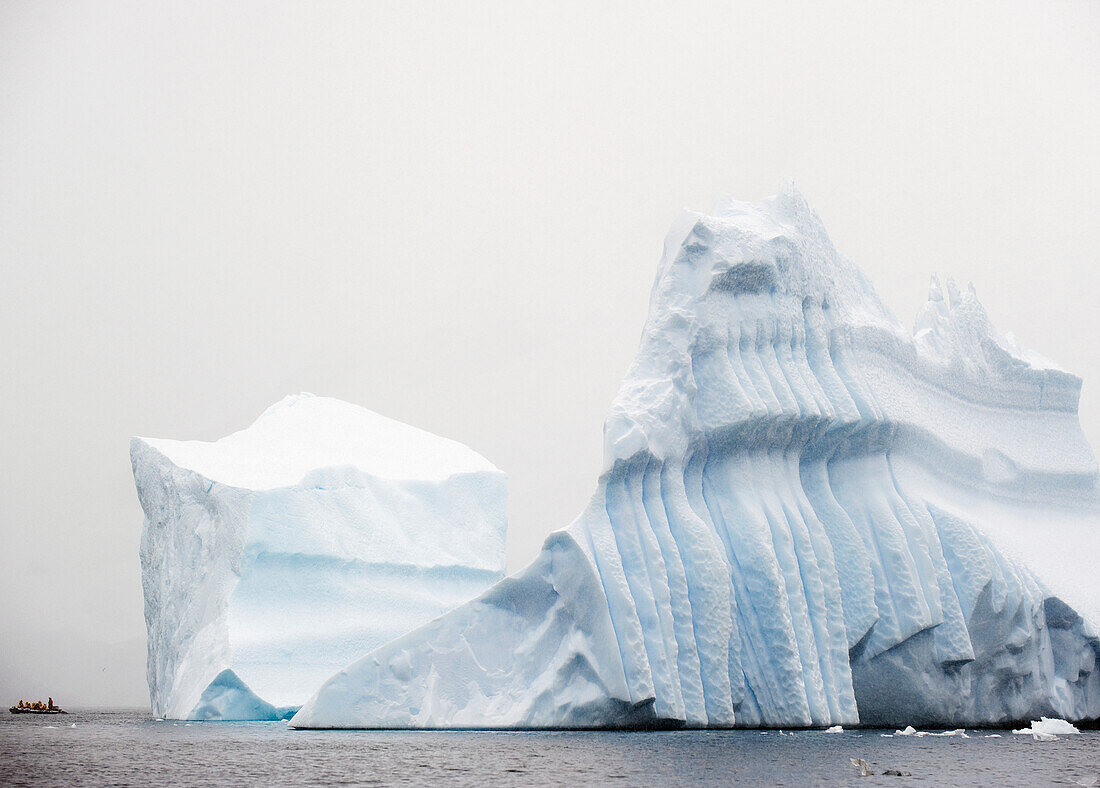 Tourists In A Boat Beside A Large Iceberg; Antarctica